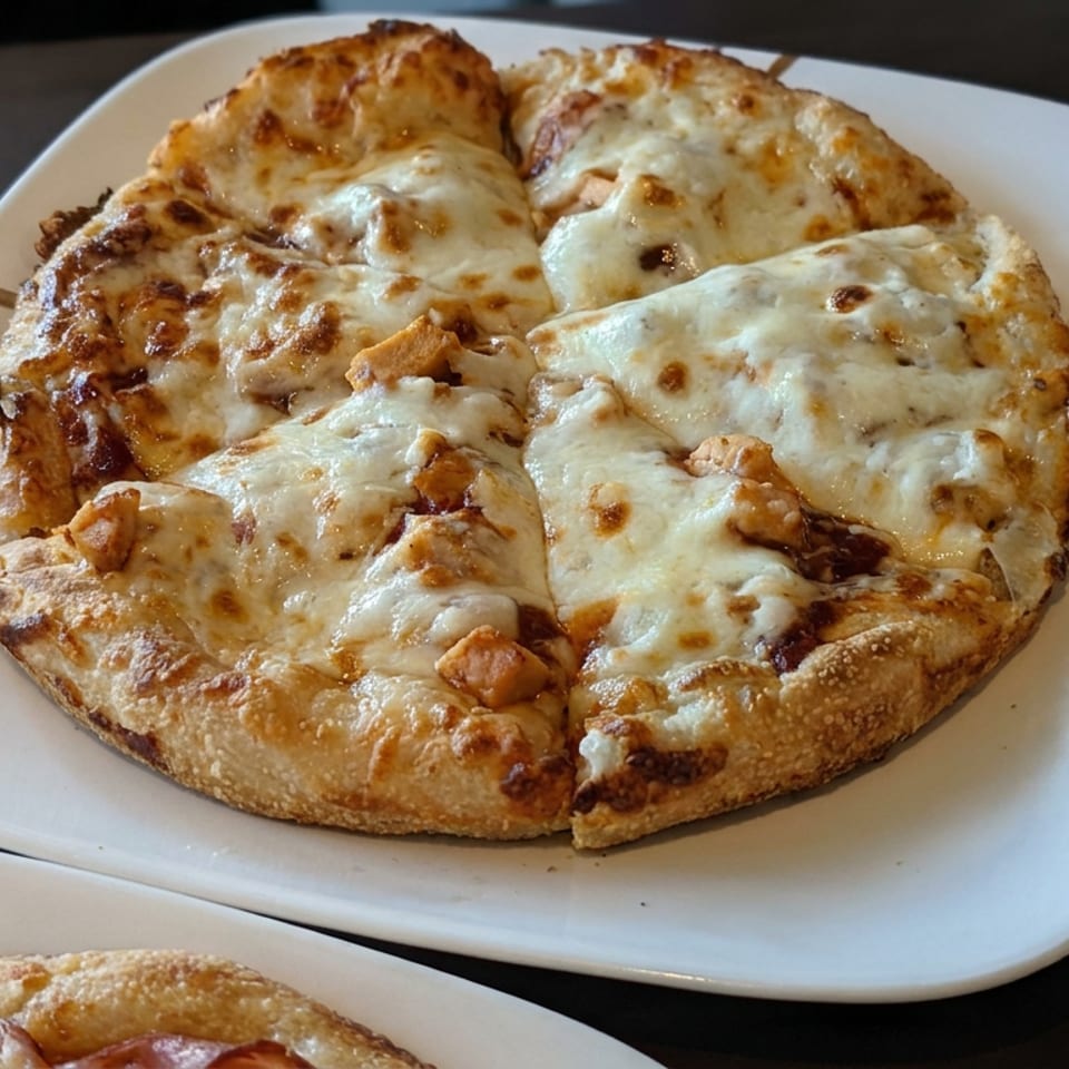 Cheese-covered pizzas with browned crusts sit on white plates atop a dark tabletop.